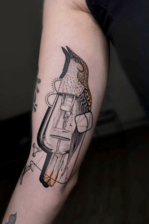 a wilga lamp bird tattoo on inner arm in black and orange done